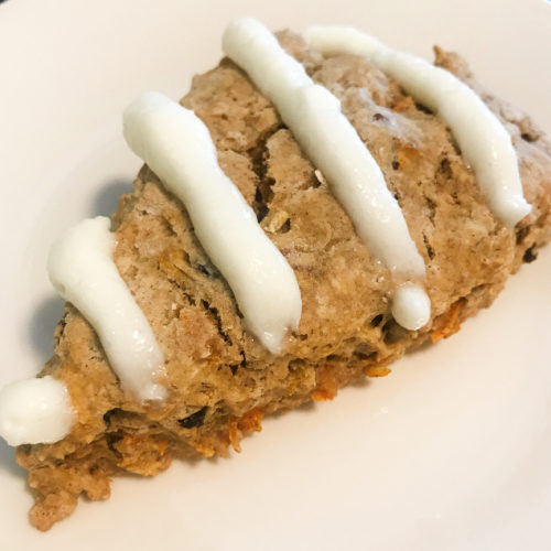 Homemade scone filled with carrots, raisins, and pecans topped with cream cheese frosting